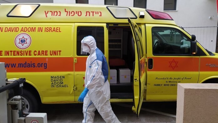 Pekerja Magen David Adom, mengenakan alat pelindung berjalan di samping unit perawatan intensif bergerak (wikipedia)