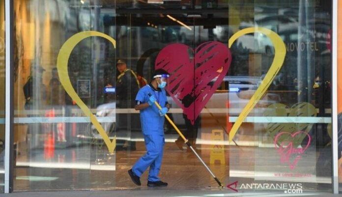 Seorang warga memakai alat pelindung diri membersihkan jalan masuk ke Hotel Novotel Melbourne South Wharf di Melbourne, Australia. ANTARA
