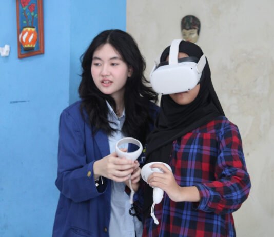 ITS Uji Coba RRekon VR, Edukasi Rekonstruksi Bencana Kini Masuk Ruang Kelas Mahasiswi ITS (kiri) ketika sedang memandu salah satu siswi SMPN 32 Surabaya saat mencoba menggunakan RRekon VR. Foto: Humas ITS